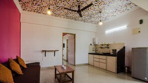 A modern kitchen with a refrigerator, microwave, and cabinets. There is a dining table with two chairs and a ceiling fan. - OYO 22730 Home Pool View 1BHK Vagator Beach (Vagator)