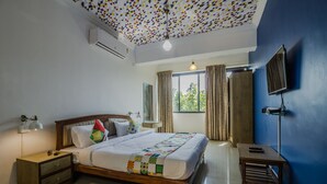 A bedroom with a wooden bed, a nightstand, a desk, a TV, and a window with curtains. - OYO 22730 Home Pool View 1BHK Vagator Beach (Vagator)