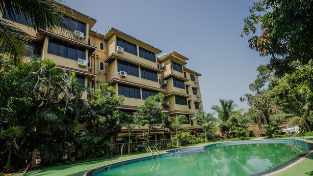 A multi-story hotel with a swimming pool surrounded by lush greenery. - OYO 22730 Home Pool View 1BHK Vagator Beach (Vagator)