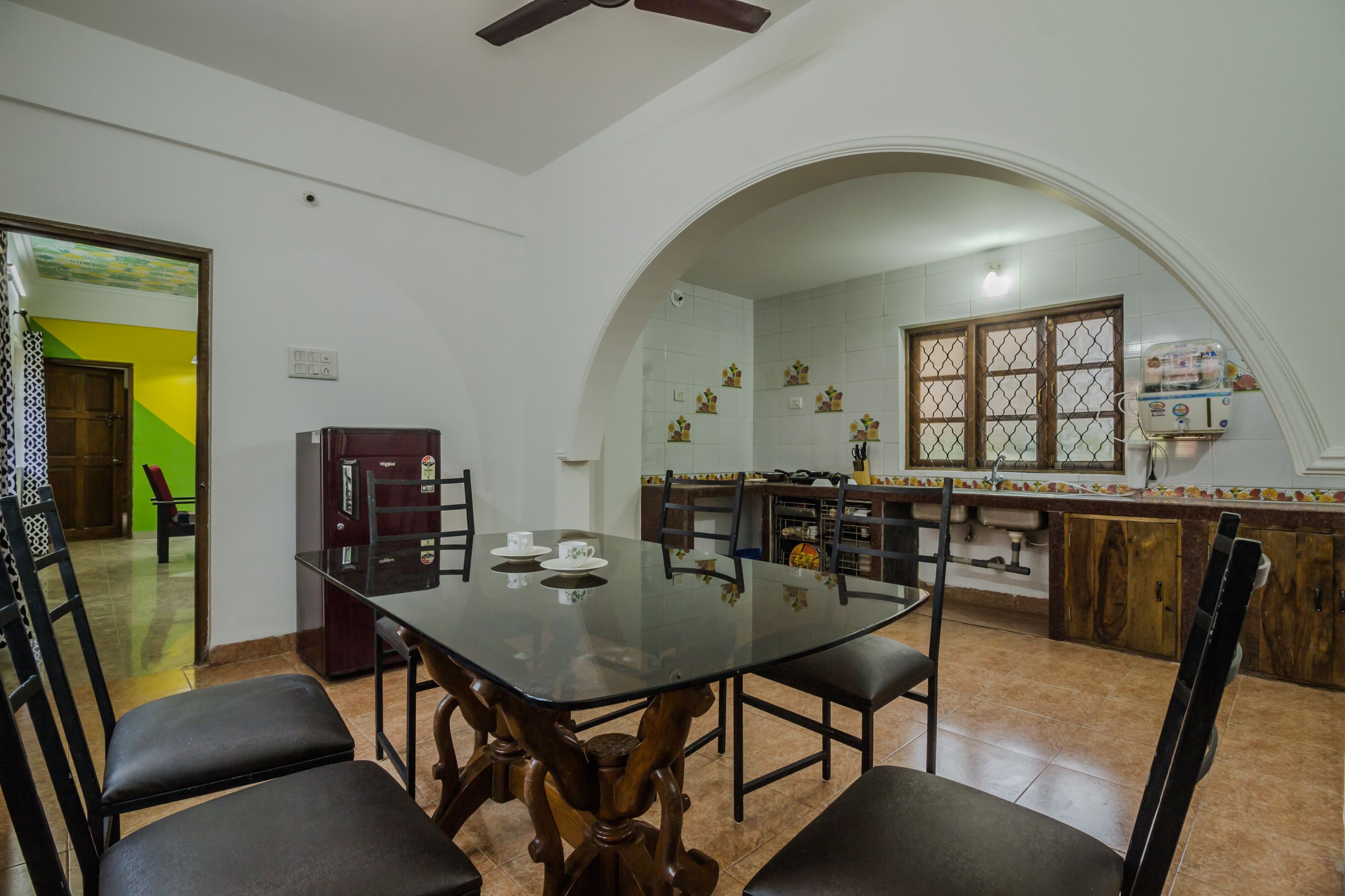 A dining area with a glass table, black chairs, and a kitchen in the background.