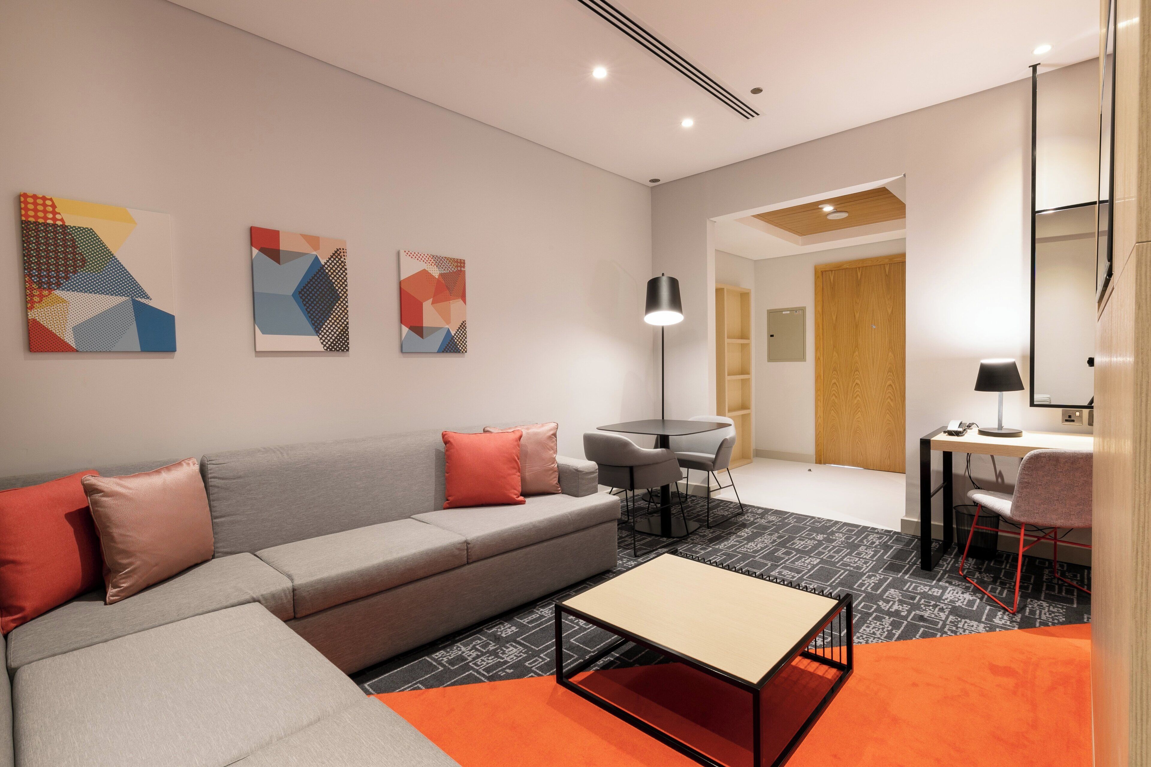 Una sala moderna con un sofá gris, alfombra naranja y arte abstracto en la pared.