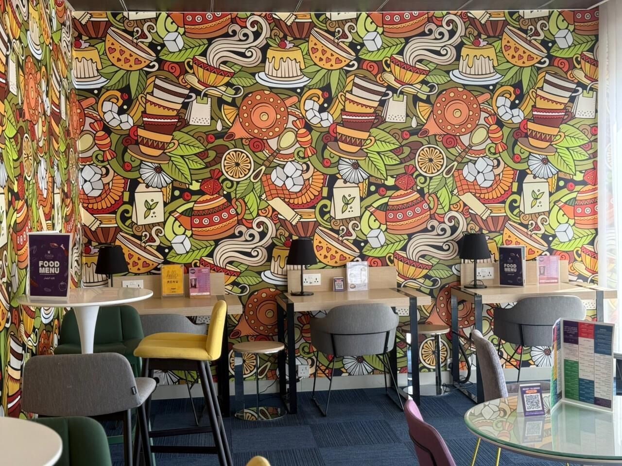 A room with a colorful, patterned wall, several tables and chairs, and a food menu sign.