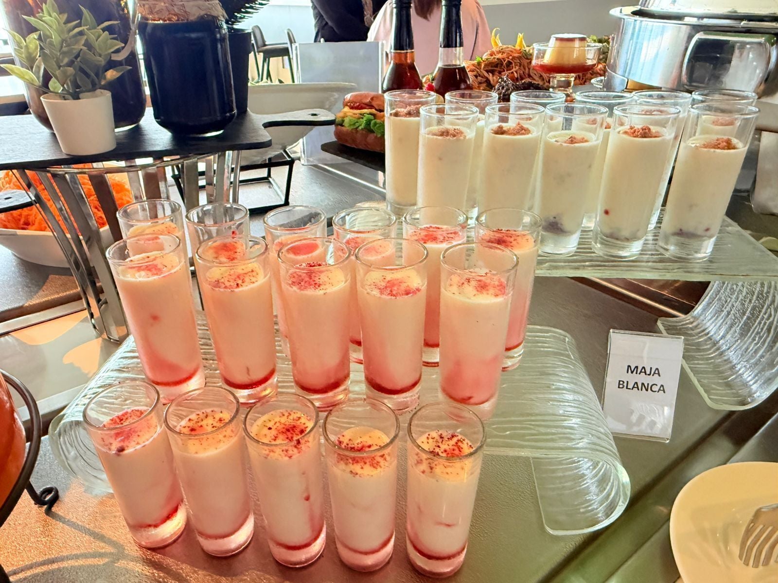 A buffet table with various food items and drinks, including a sign for 'MAJA BLANCA'.
