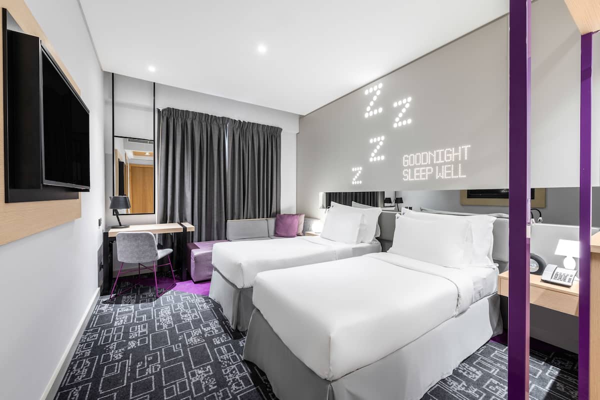 Ein Hotelzimmer mit zwei Betten, einem Schreibtisch, einem Stuhl, einem Fernseher und einer Wand mit beleuchtetem Text.