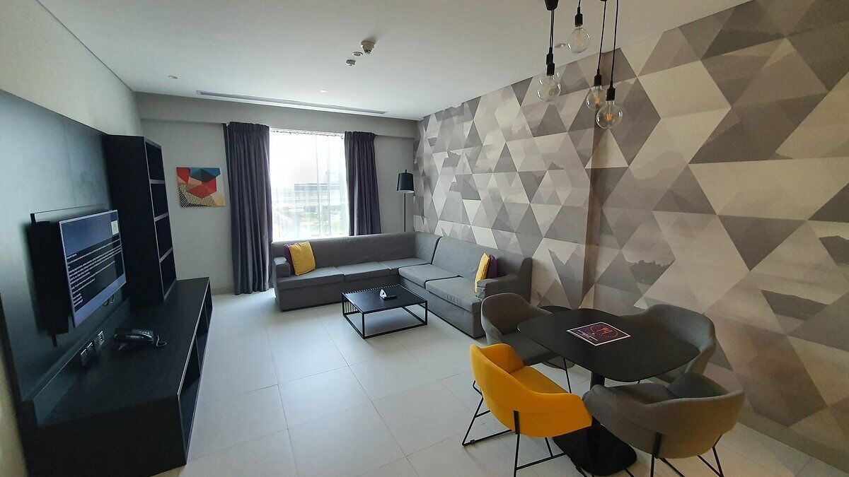 Ein modernes Wohnzimmer mit einer Couch, einem Esstisch mit Stühlen, einem Fernseher und einer Wand mit geometrischem Muster.