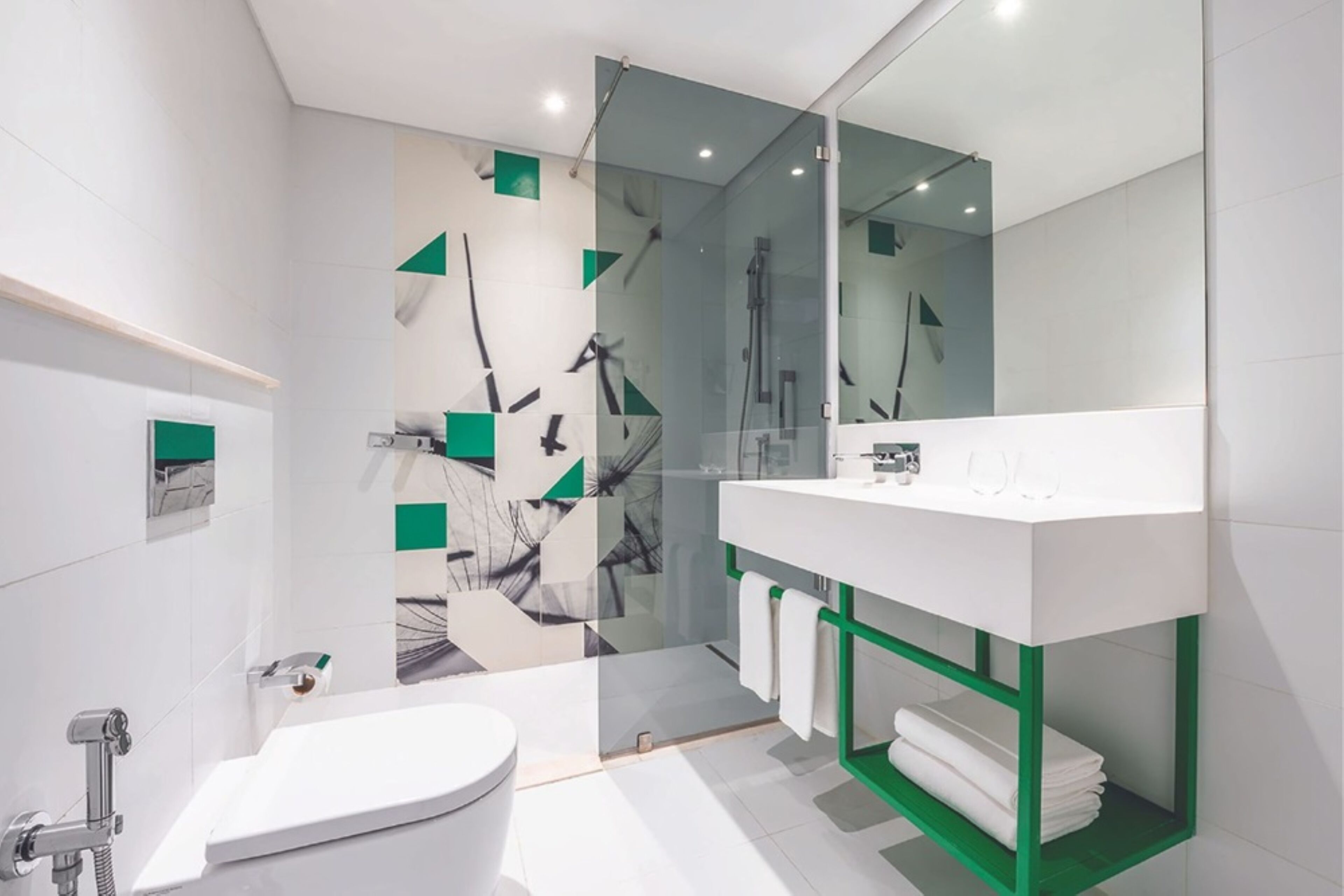 Et moderne badeværelse med toilet i hvidt, bruseniche i glas og et hvidt håndvaskskab med en grøn hylde.