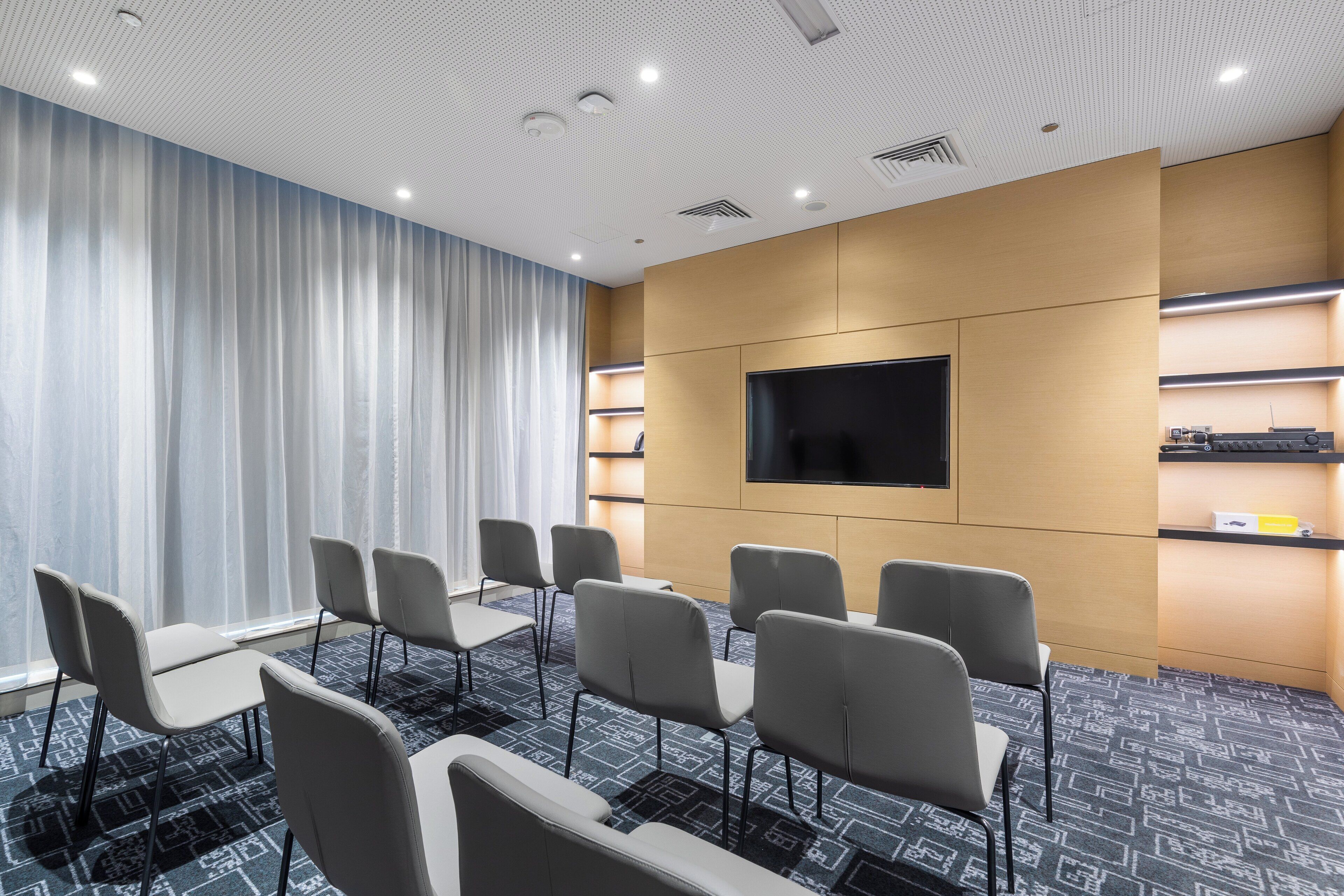 A conference room with a large TV screen, rows of chairs, and a patterned carpet.