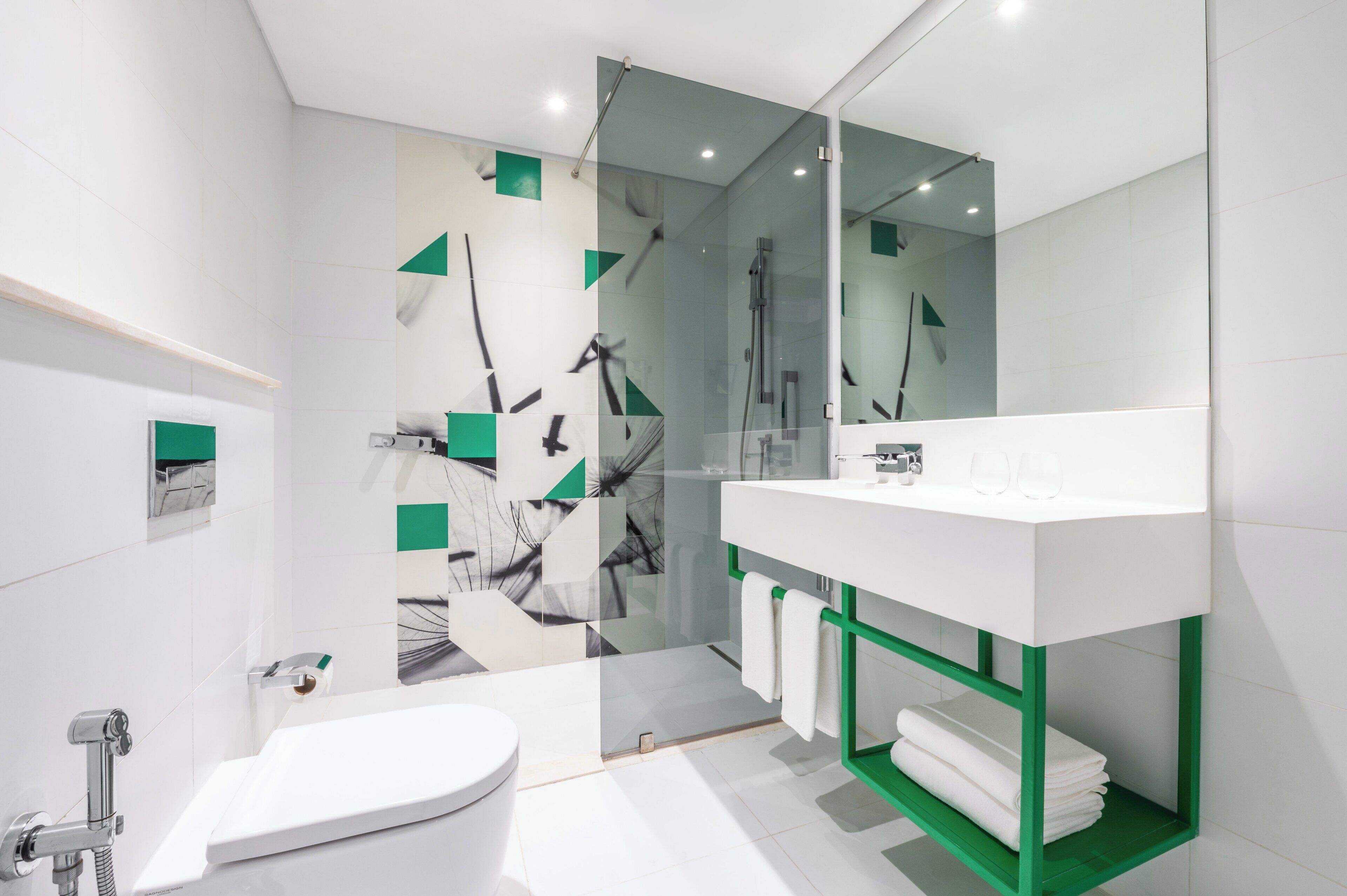 A modern bathroom with a white sink, green towel rack, and a glass shower enclosure.
