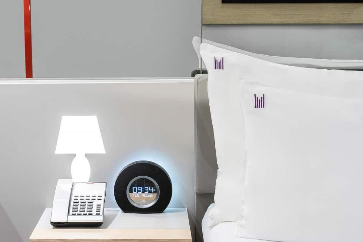 Ein Hotelzimmer mit einem Nachttisch, der eine Lampe, eine digitale Uhr und ein Telefon zeigt.