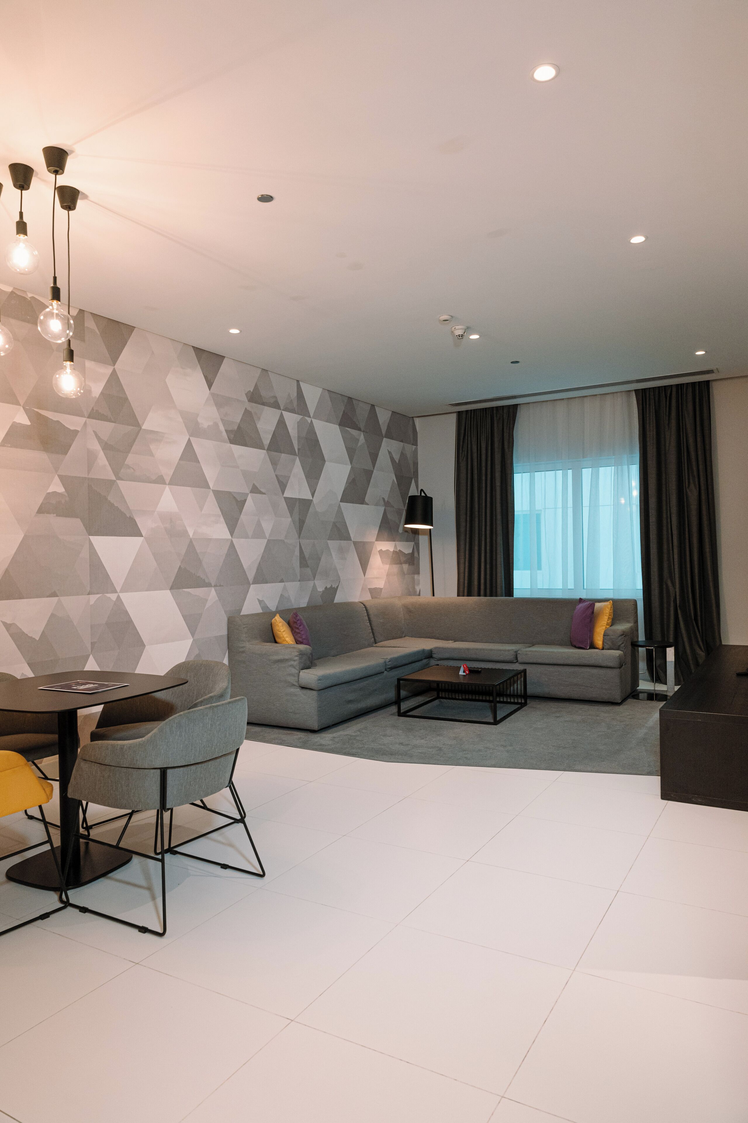 A modern living room with a gray sectional sofa, a coffee table, and a dining area with chairs.