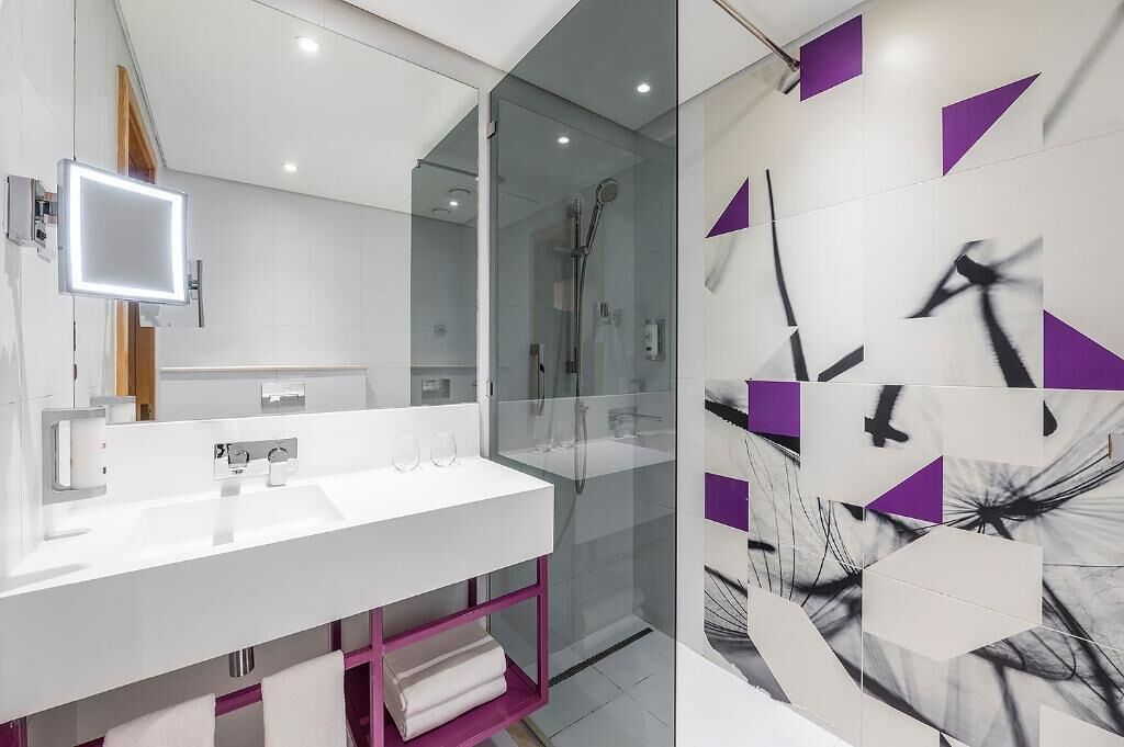 Ein modernes Badezimmer mit einem weißen Waschbecken, einem Spiegel und einer Duschkabine aus Glas.