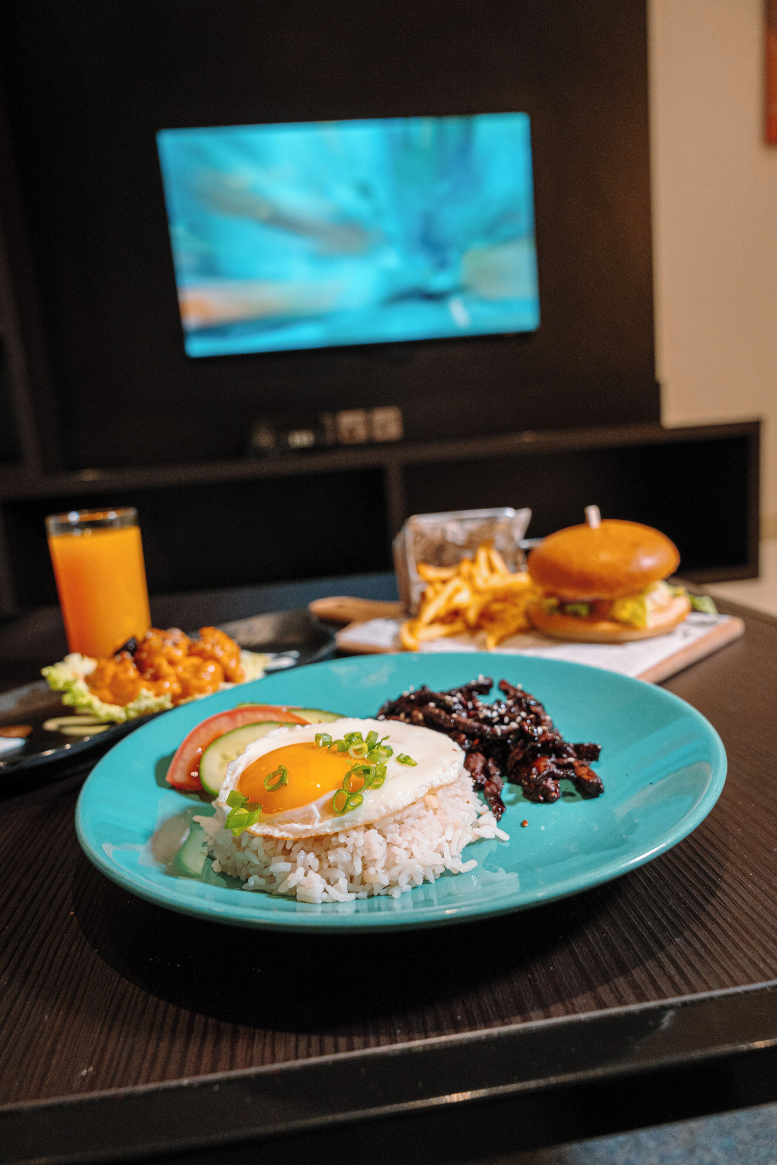 Una mesa de comedor con un plato de comida, un vaso de jugo de naranja y una hamburguesa.