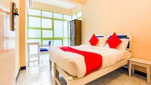 A hotel room with a large bed, a bedside table, and a chair. There is a window with green frames and a view of the outside. - OYO 776 Royal Heritage (Calangute)