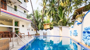 A pool area with a clear blue pool, wooden deck, and chairs. - OYO 776 Royal Heritage (Calangute)