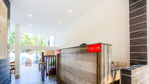 A hotel reception area with a check-in/check-out desk, wooden flooring, and a view of the outdoor seating area. - OYO 776 Royal Heritage (Calangute)