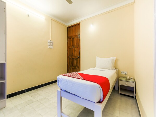 Un dormitorio con cama, mesita de noche, puerta de madera y un interruptor de luz en la pared.