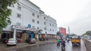 Un edificio blanco con un letrero del Metro Grand Hotel, coches estacionados, motocicletas y un camión amarillo en una calle mojada.