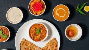 Variedad de platos de la cocina india, incluyendo curry, pan naan y un tazón de sopa, sobre una superficie oscura.