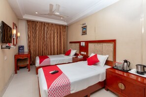 A hotel room with two beds, a TV, a ceiling fan, a minibar, and a large window with curtains. - Edition O 30030 Hotel Metro Grand (Chennai)