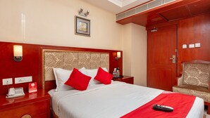 Una habitación de hotel con una cama grande, ropa de cama roja y blanca, una mesita de noche con un teléfono y una silla.