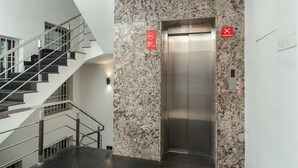 A modern elevator with a marble wall, a staircase with glass railings, and a 'No Smoking' sign.