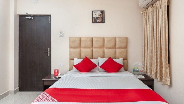 A hotel room with a bed, a nightstand, a door, and an air conditioning unit.
