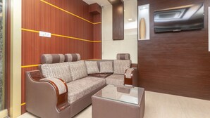A modern living room with a sectional sofa, a glass coffee table, and a flat-screen TV mounted on the wall.