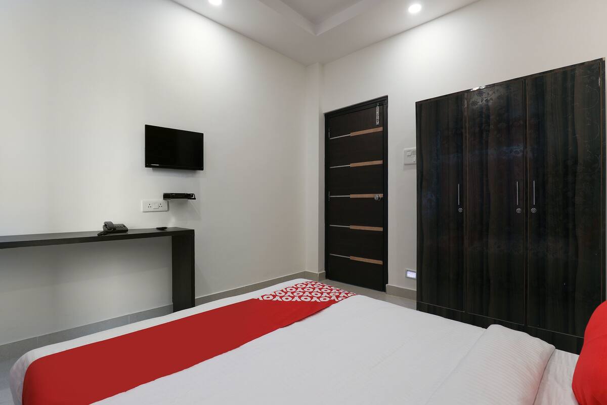 Een slaapkamer met een bed, bureau, televisie en een kledingkast.