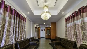 A hotel lobby with leather sofas arranged in rows, a chandelier, patterned curtains, and a sign with the name 'OYZ'. - OYO 14184 Hotel Green Stone (Hyderabad)