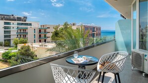 A balcony with a table, two chairs, and a view of the sea and buildings. - Maison 66 Riviera Hotels (Alimos)