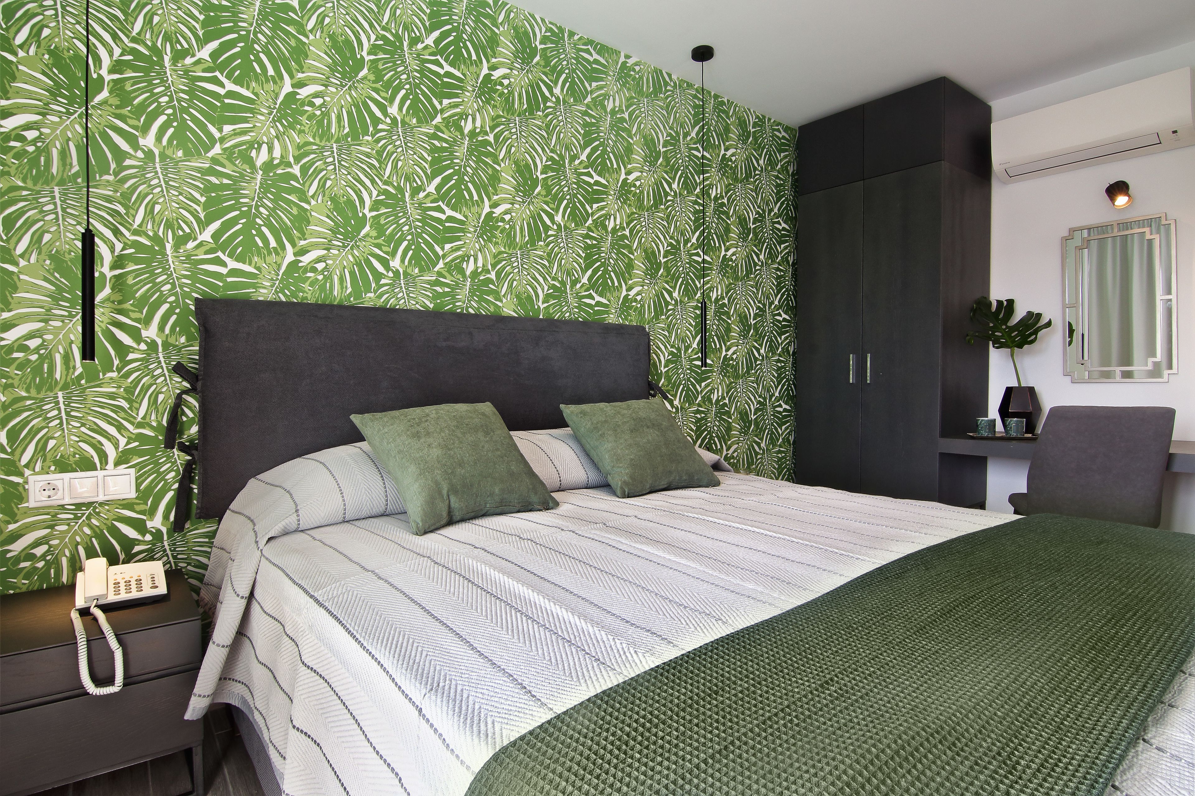 A bedroom with a bed, green pillows, a nightstand with a phone, and a plant.