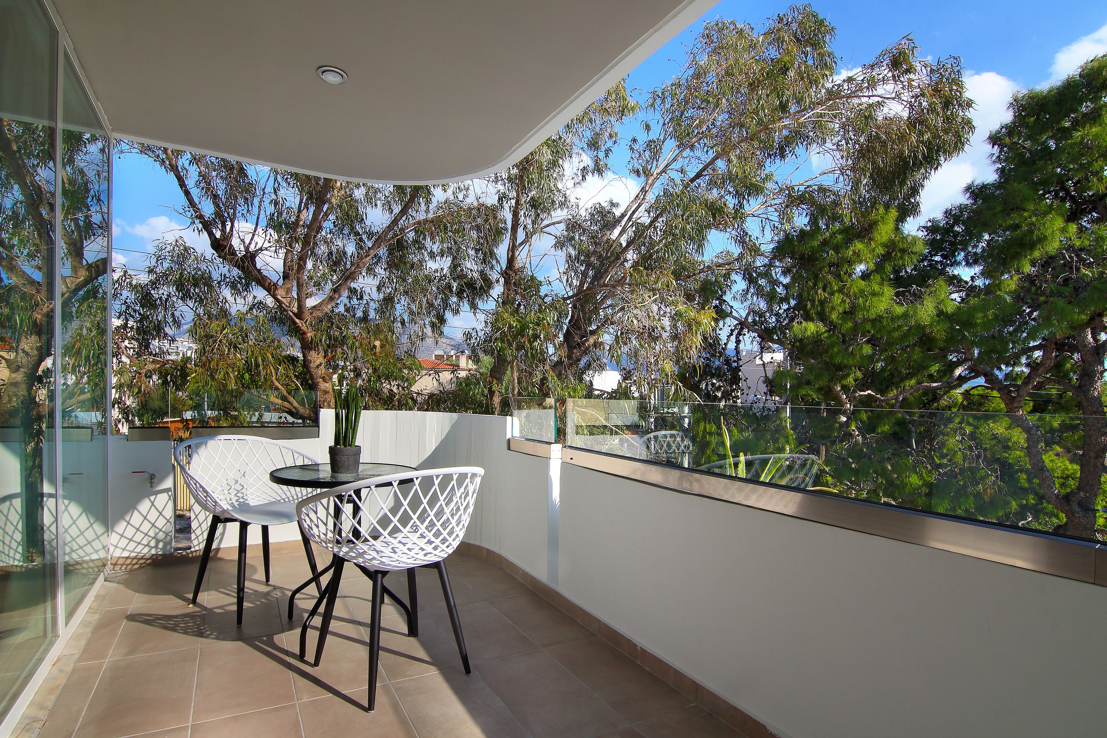 A balcony with a glass railing, white chairs, and a table.