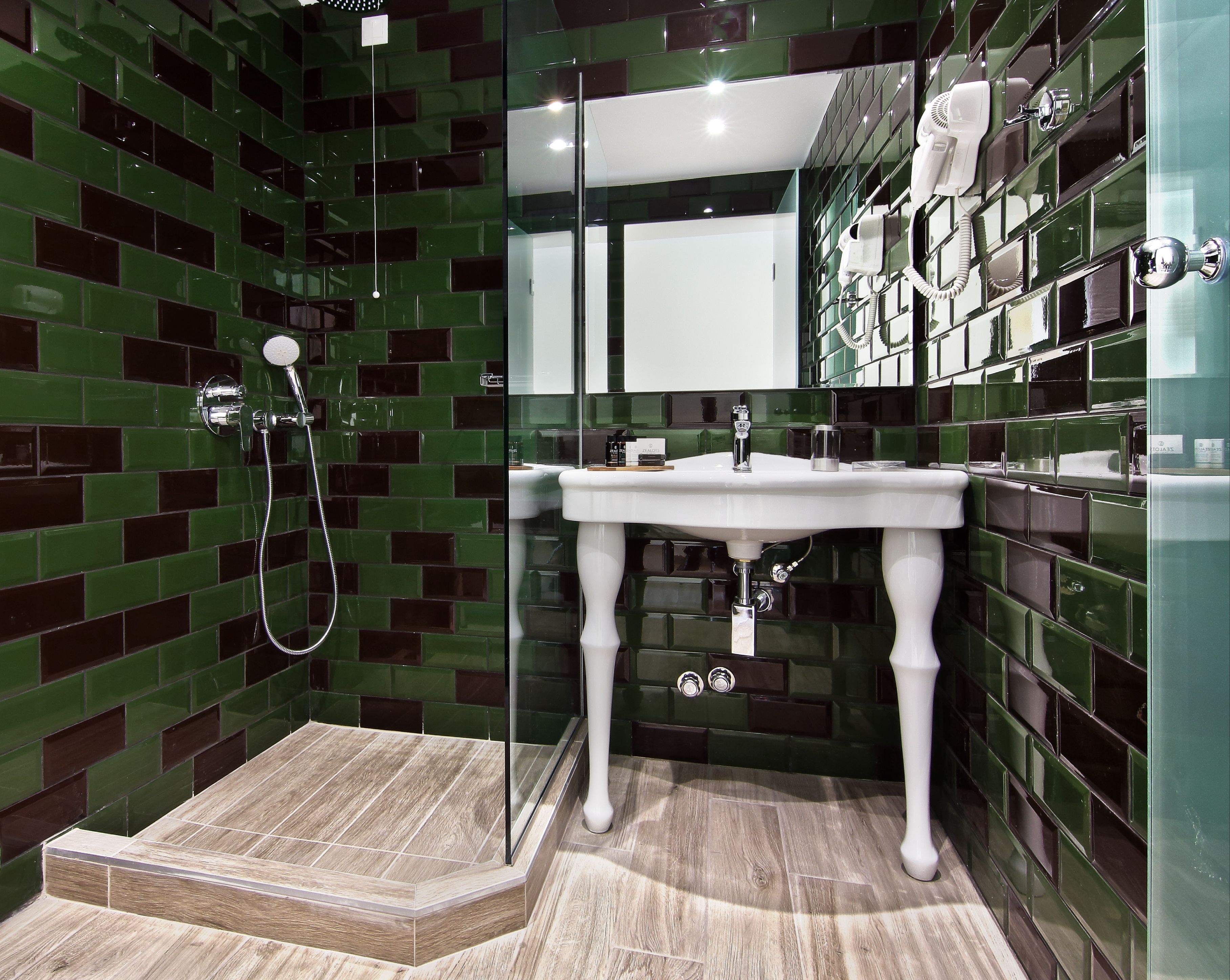 Un baño con un lavamanos blanco, paredes con azulejos verdes y zona de ducha.