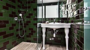 Un baño con un lavamanos blanco, paredes con azulejos verdes y zona de ducha.