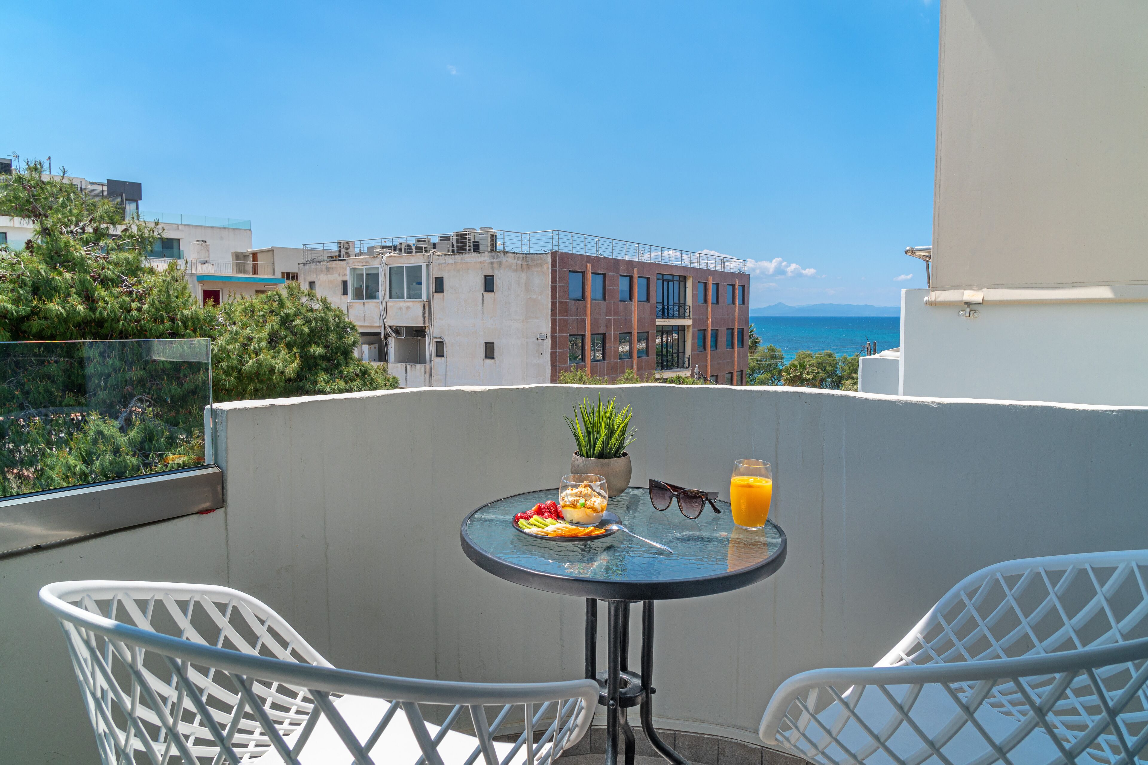 A balcony with a table set for breakfast, including a plate of food, a glass of orange juice, and a potted plant.