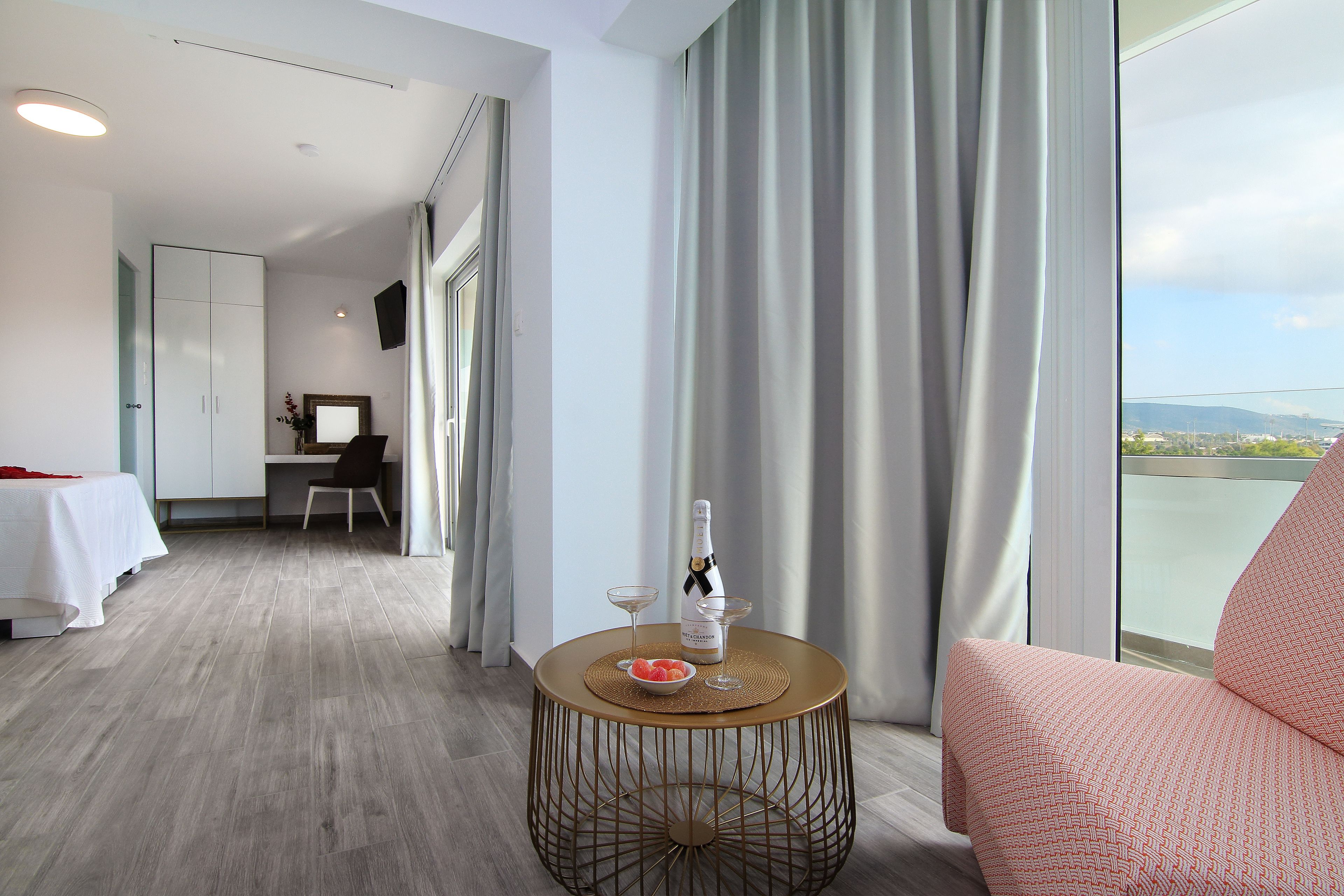 Une chambre d’hôtel avec un lit, une table basse ronde sur laquelle se trouvent une bouteille et des verres, une chaise, et une vue sur l’extérieur.