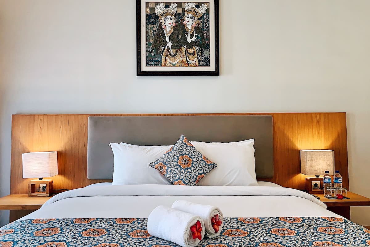 A neatly made bed with patterned bedding, two bedside lamps, and a framed artwork above the bed.