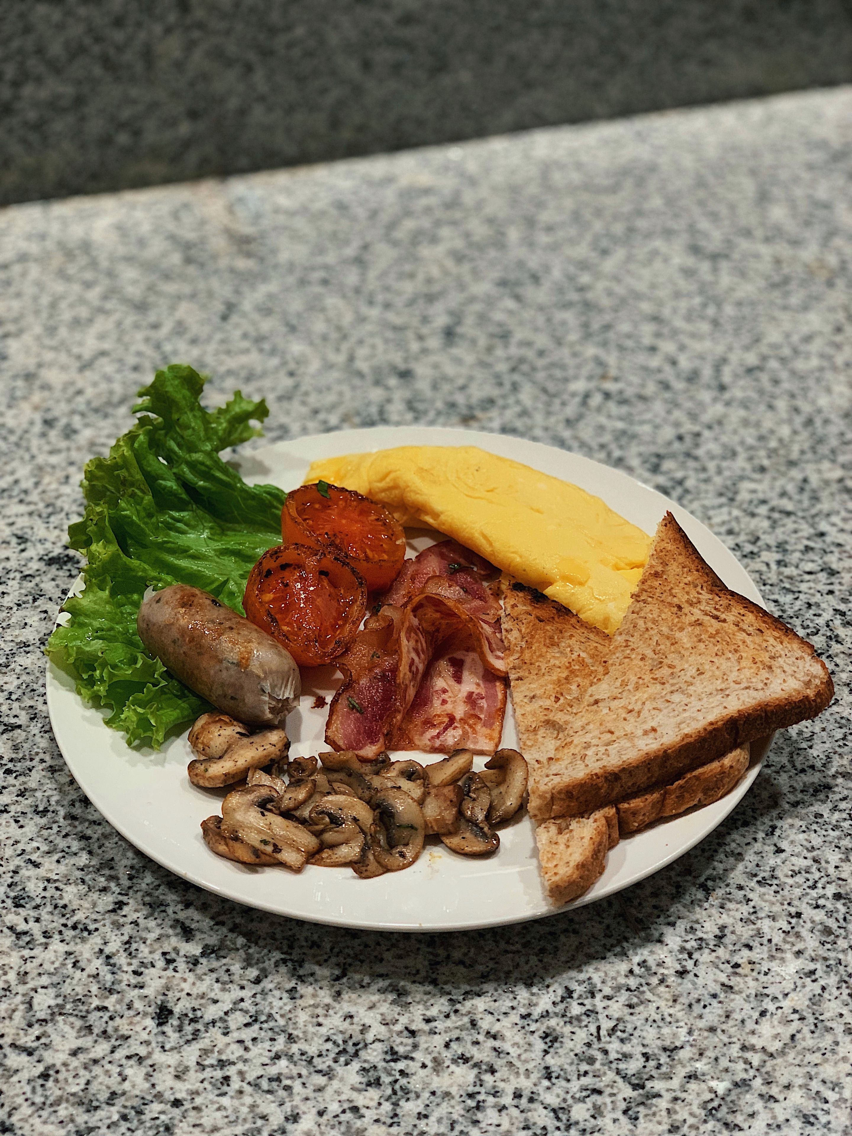 Un plato de comida para el desayuno con tostadas, huevos, tocino, champiñones y tomate.