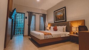 A hotel room with a large bed, a desk, a chair, a nightstand, and a painting on the wall. - Perissos Echo Beach (Canggu)
