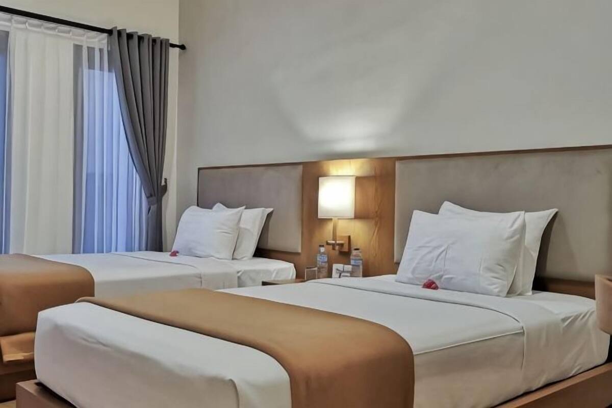 A hotel room with two beds, a nightstand with a lamp, and a window with curtains.