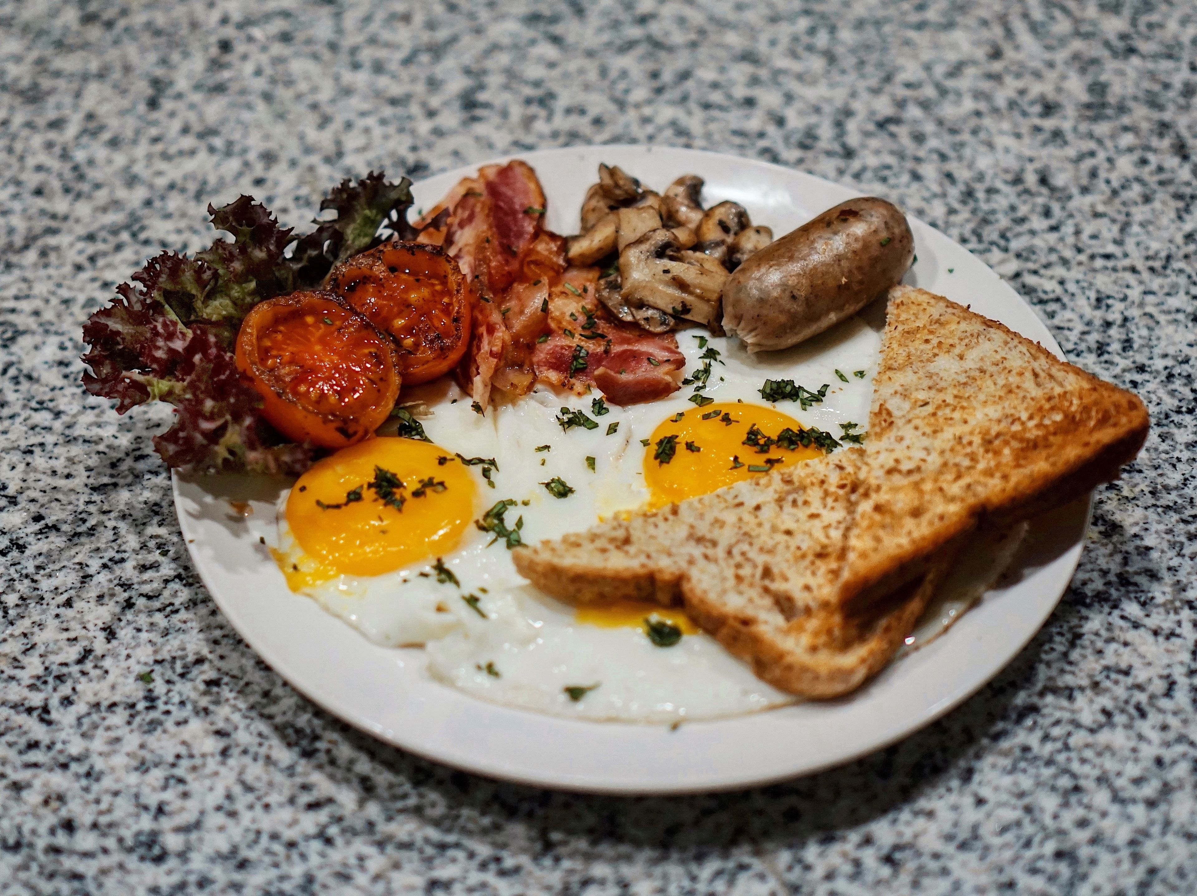 A plate of breakfast food including eggs, bacon, mushrooms, sausages, and toast.