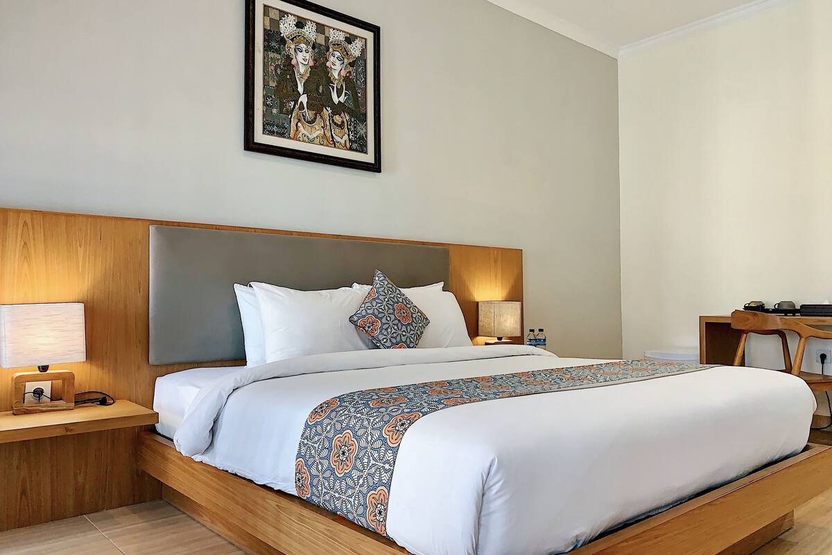 A hotel room with a large bed, two bedside tables with lamps, a wooden headboard, and a framed artwork above the bed.