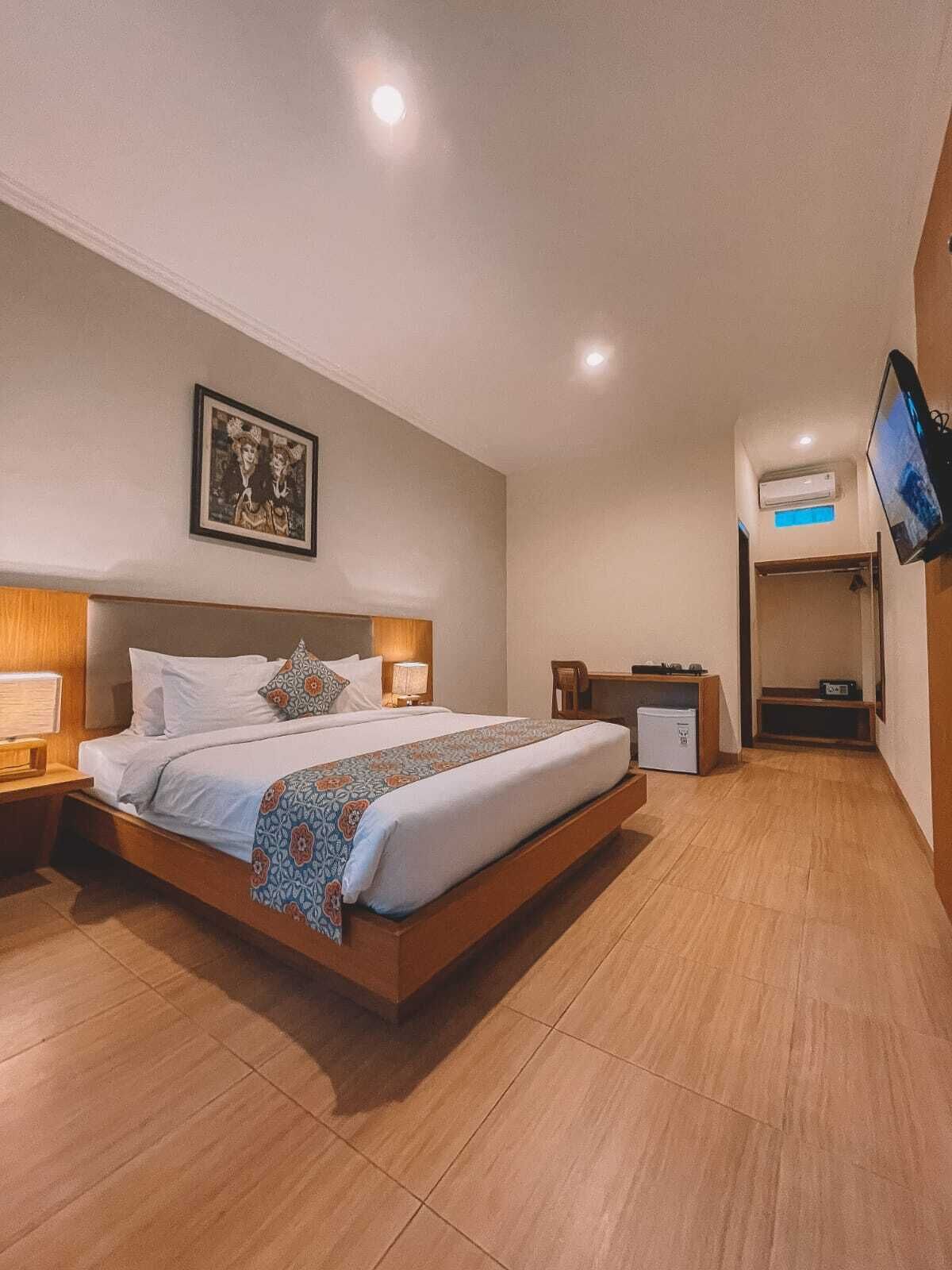 A modern hotel room with a large bed, bedside tables, a flat-screen TV, an air conditioning unit, and a framed picture on the wall.