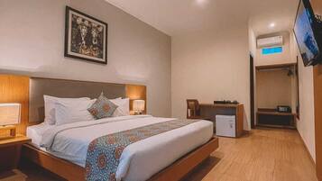A modern hotel room with a large bed, bedside tables, a flat-screen TV, an air conditioning unit, and a framed picture on the wall.