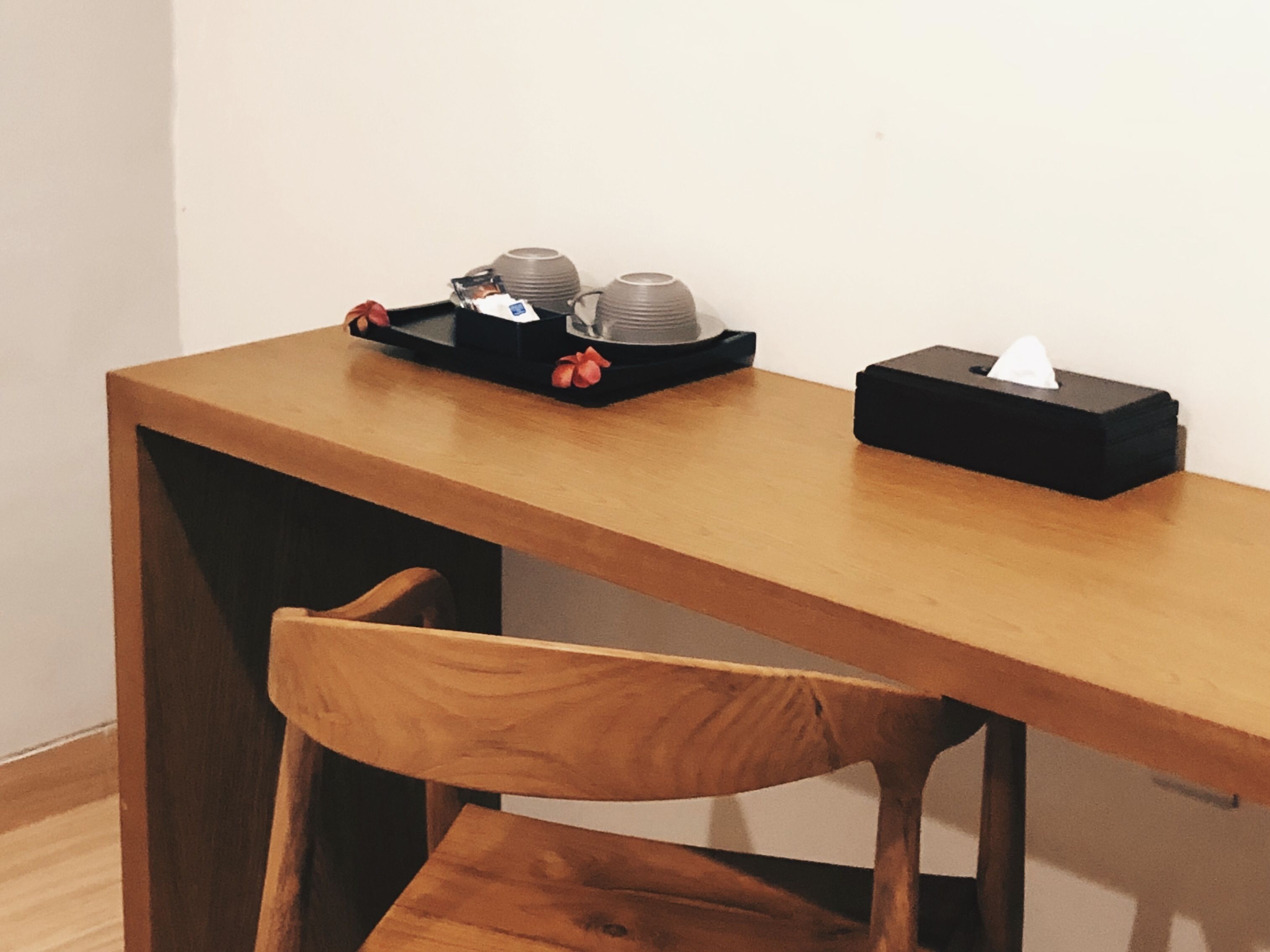 Een houten tafel met een zwarte dienblad waarop een zakvochtige papieren zakdoos en een stapel bekers staan.