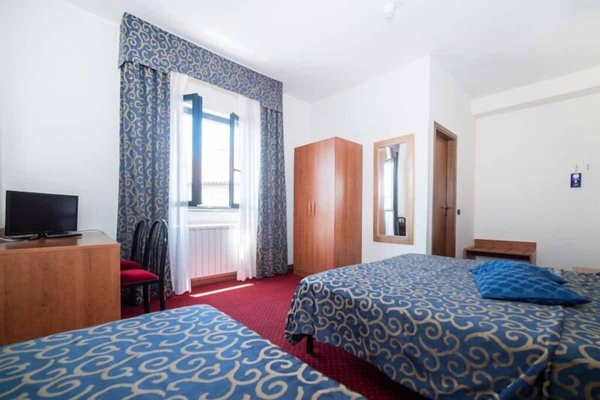 A hotel room with two beds, a TV, a wardrobe, and a window with curtains.