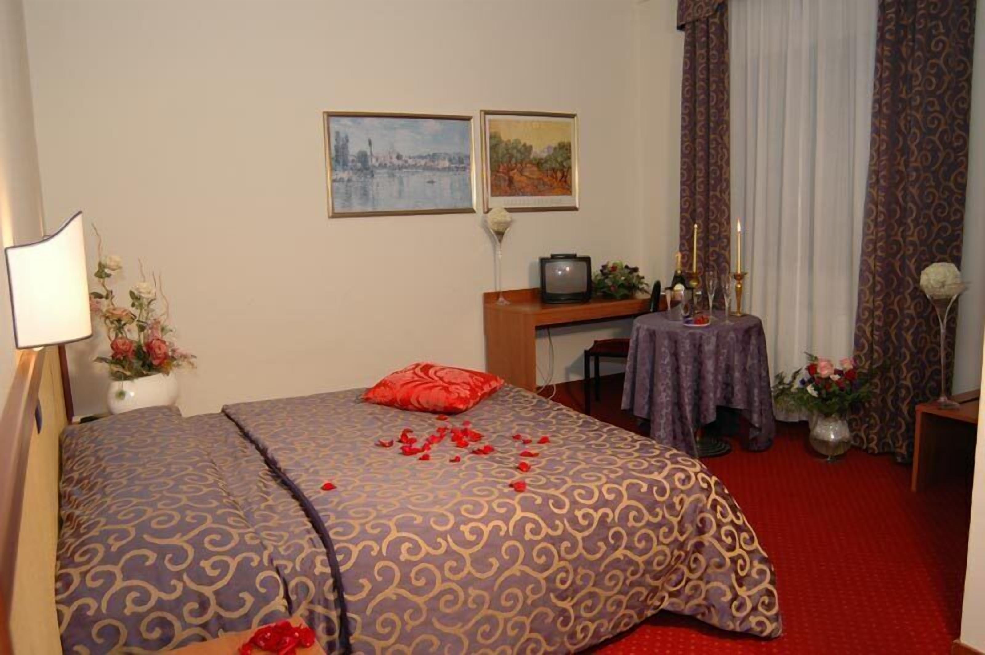Une chambre d’hôtel avec deux lits, un bureau, une télévision et une petite table sur laquelle est posé un vase de fleurs.