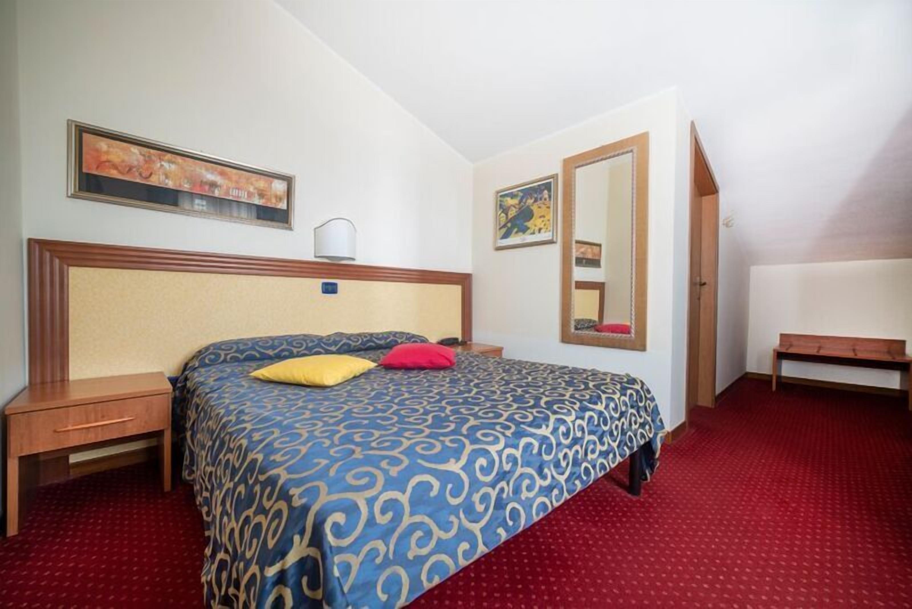 Une chambre d’hôtel avec un grand lit, une table de chevet, une commode, un banc et un miroir au mur.