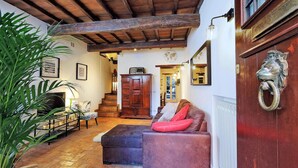 A cozy living room with a wooden ceiling, a fireplace, a sofa, and a large plant. - San Callisto - WR Apartments (Rome)
