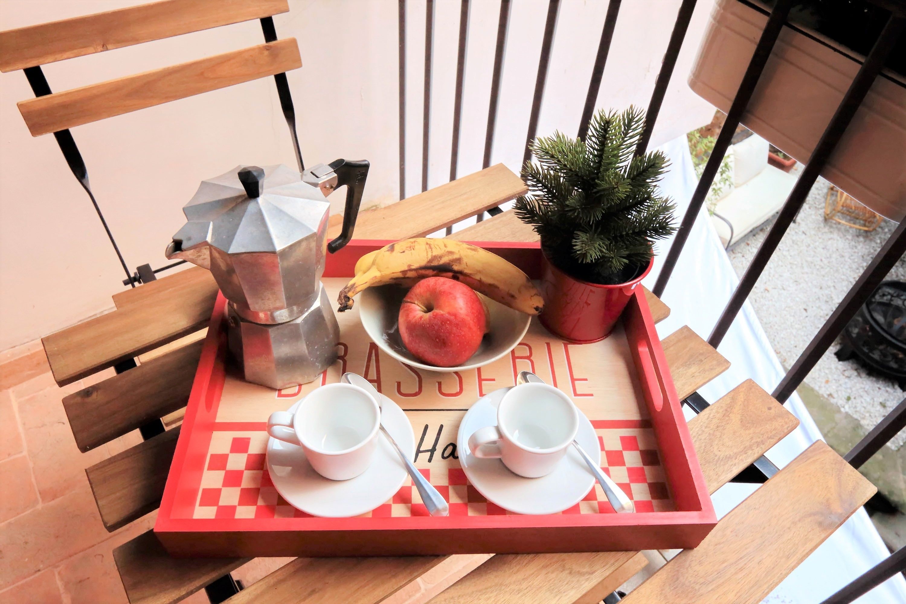 A tray with a coffee pot, a banana, an apple, and a small potted plant on a checkered table.
